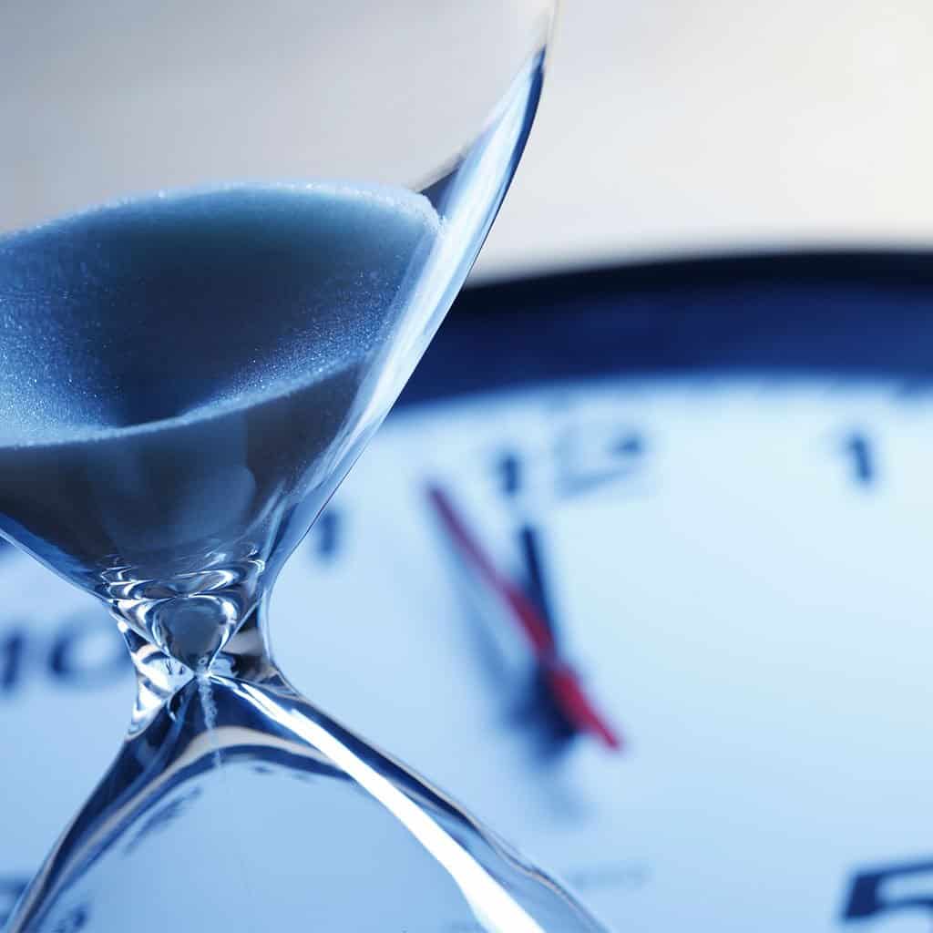 Sand timer with blurred clock background representing fast turnaround service